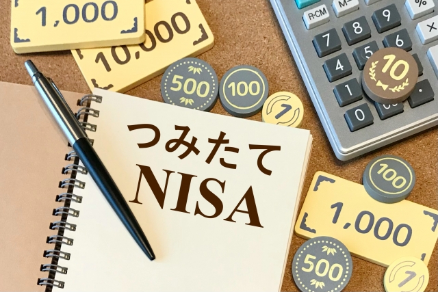 つみたてNISAと書かれたメモ帳とお金を模したおもちゃ