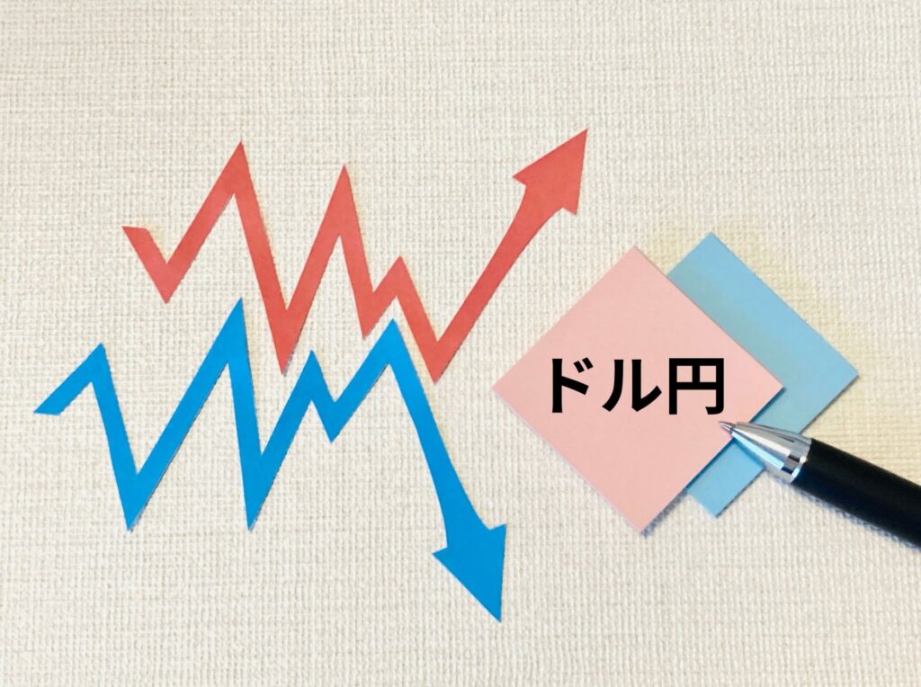 ジグザグしながら上昇する赤い矢印と青い矢印、ドル円と書かれた四角い紙とペン