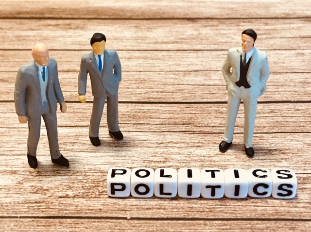 POLITICSと書かれたサイコロの近くにスーツを着た人形が3体立っている