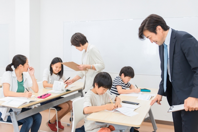 小学生に勉強を教える塾講師2人と机に座って勉強する生徒4人